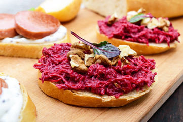 Breakfast sandwiches with boiled grated beets and walnuts on a piece of white baguette on a cutting board.