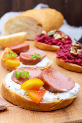 Sandwiches for breakfast with fried sausages, yellow tomatoes, creamy mustard sauce on a cutting board. Vertical view