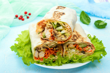 Shawarma - Middle Eastern dish made from lavash (pita), stuffed with chicken, mushrooms, fresh vegetable salad, sauce. Serving on lettuce leaves on a light background. The top view.