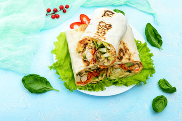 Shawarma - Middle Eastern dish made from lavash (pita), stuffed with chicken, mushrooms, fresh vegetable salad, sauce. Serving on lettuce leaves on a light background. The top view.