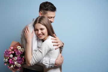 Happy young couple with bouquet of flowers on light background
