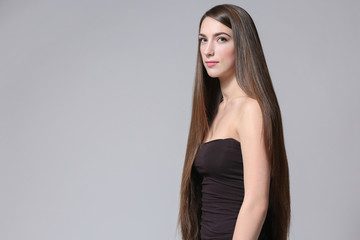 Naklejka premium Beautiful young woman with long straight hair on light background