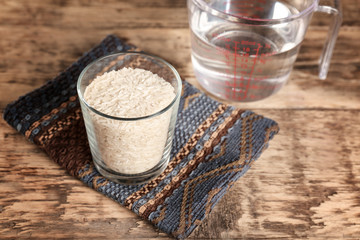 Glass of rice and measuring jug with water on wooden table