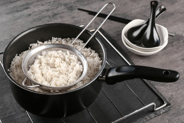 Cooked rice in saucepan with sifter on grate