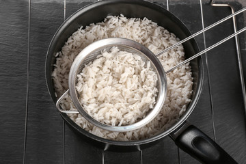 Cooked rice in saucepan with sifter on grate