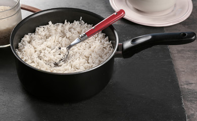 Cooked rice in saucepan with spoon on slate board