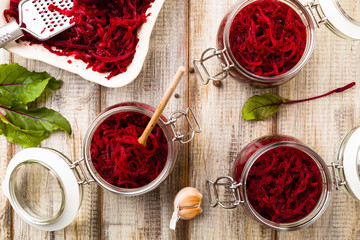 Grated beetroot marinated in jars. Wooden background.