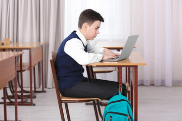 Incorrect posture concept. Schoolboy sitting at desk in classroom