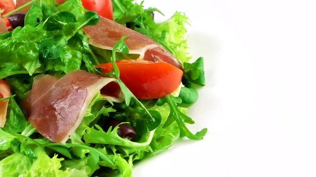 Edge of plate with Restaurant salad, copy space in right side, ham (Sliced Spanish), lettuce leaf, arugula, tomatoes and olives, loop
