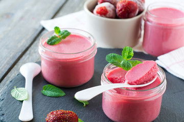 Strawberry mousse in glass jars and frozen strawberries on an old wooden table background. Selective focus.
