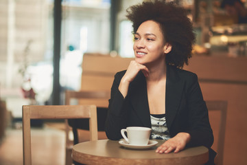 Mixed race woman in coffee shop having coffee and smiling