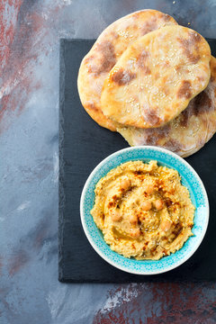 Hummus, chickpeas, with spices and pita, flat cake in a plate on a background of gray stone. Selective focus.