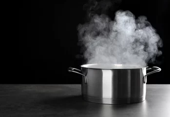 Poster Metal saucepan with hot liquid on table against dark background © Africa Studio
