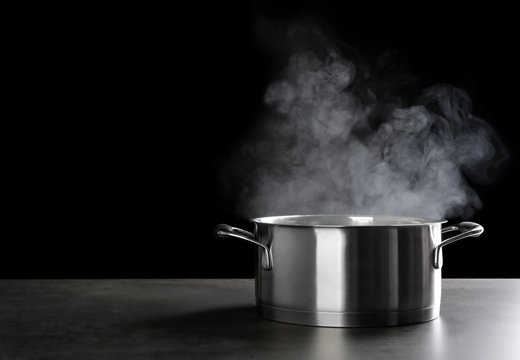 Metal saucepan with hot liquid on table against dark background