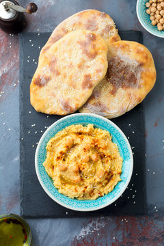 Hummus, chickpeas, with spices and pita, flat cake in a plate on a background of gray stone. Selective focus.
