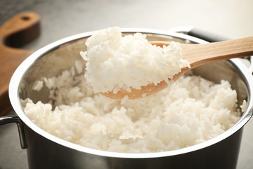 Spoon with cooked rice over metal saucepan, closeup