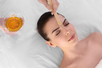 Beautician depilating young woman's face with wax in spa center