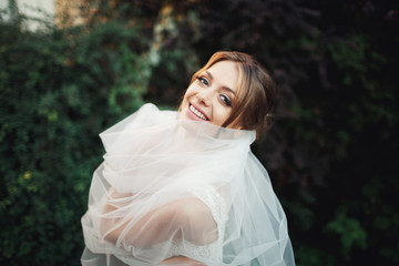 Joyful bride with tender pink lips covers herself in the veil