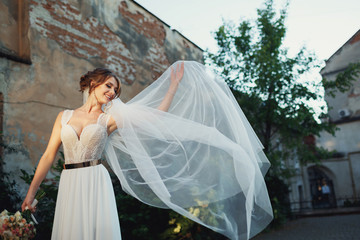 Bride in lace corset holds her veil up posing on the street