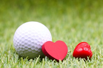 Naklejka premium golf ball with red heart are on green grass