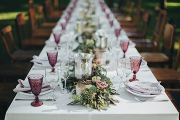 Festive table served dishes and decorated with branches of greenery, stands on green grass in the area of wedding party