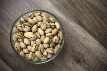 Glass bowl of pistachios on wooden background