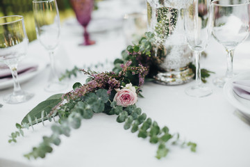 Festive table served dishes and decorated with branches of greenery, stands on green grass in the area of wedding party