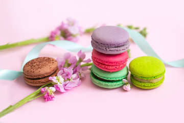 Multicolored macaroons сakes, straws for juice and flowers on a pink background.