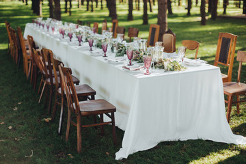 Festive table served dishes and decorated with branches of greenery, stands on green grass in the area of wedding party