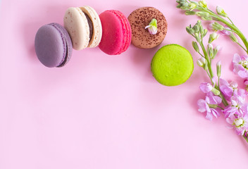 Obraz premium Multicolored macaroons сakes and flowers on a pink background.