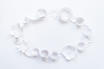 Oval frame with white paper flowers on white background.