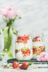 Healthy spring breakfast. Greek yogurt, granola, strawberry breakfast jars, pink raninkulus flowers, marble background, selective focus, copy space. Clean eating, diet, detox vegetarian food concept