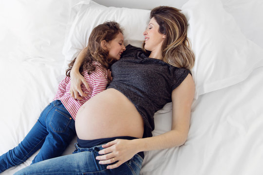 pregnant woman and her little girl lying on a bed cuddling and laughing together