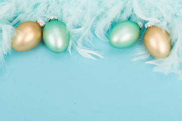 Decoration glass yellow and green easter eggs and blue feathers on a blue background with space for text