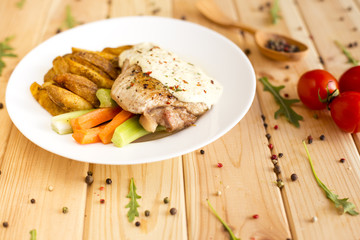 Fillet of turkey with vegetables on a white plate. Wooden background