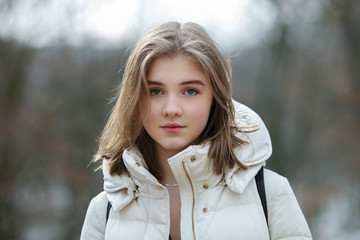 Headshot of beautiful young natural looking blonde woman posing on the spring city park in warm clothes. Positive emotions lifestyle concept