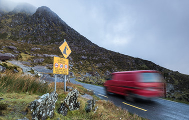 Motion blur of Van driving past Road warning sign on Conor Pass in the Dingle Peninsula, County...