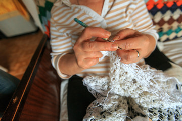 Obraz premium Female hands knit white scarf by green hook. Close-up knitting for background.