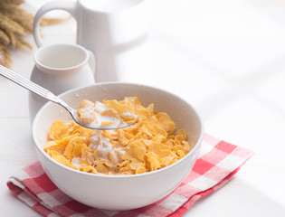 Corn flakes with jug of milk on table wooden,shadows from a window frame