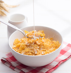 Pouring milk into Corn flakes with jug of milk on table wooden,shadows from a window frame