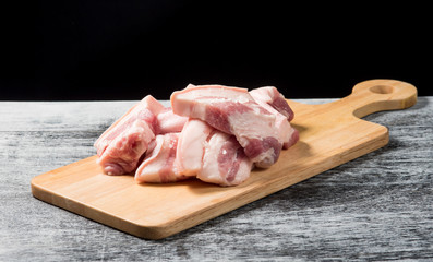 Pork belly on a wooden board over black background.