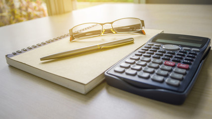 The desk have empty notebook, eyeglasses and calculator on the wooden table.