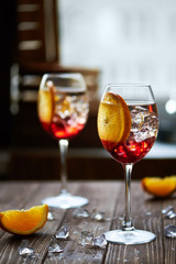 refreshing red cocktails with orange isolated on a wooden background with oranges and ice against big window