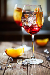 Two refreshing red cocktails with orange isolated on a wooden background with oranges and ice with backlight