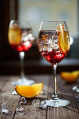 Two refreshing red cocktails with orange isolated on a wooden background with oranges and ice with backlight