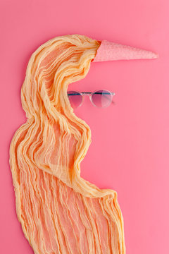 Composition of pink waffle ice cream cones with yellow fabric in the form of hair and glasses creating the outline of a girl
