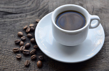 Coffee cup with beans on old rustic wooden table.White coffee mug.Morning coffee or breakfast concept.Selective focus.