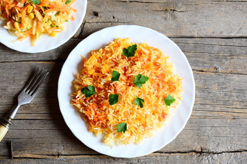 Healthy basmati rice with vegetables and parsley on a plate, cabbage salad on a plate, fork on vintage wooden table. Vegan lunch or dinner recipe. Top view