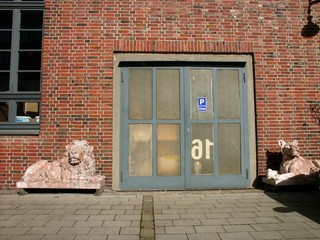 Löwenstatue vor einer alten braunen Backsteinfassade mit Garagentor in einem Hinterhof bei...