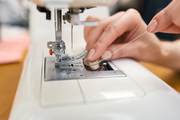 Fototapeta na wymiar Female tailor threading bobbin into sewing machine case